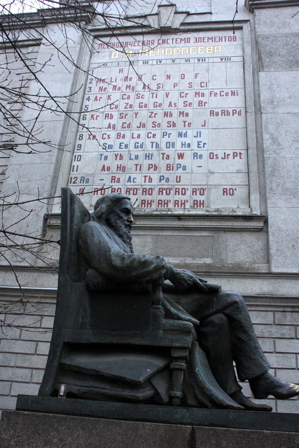 Photograph of a tall stone monument and a large mosaic of the Periodic Table on the side of a building, dedicated to Dmitri Mendeleev.
